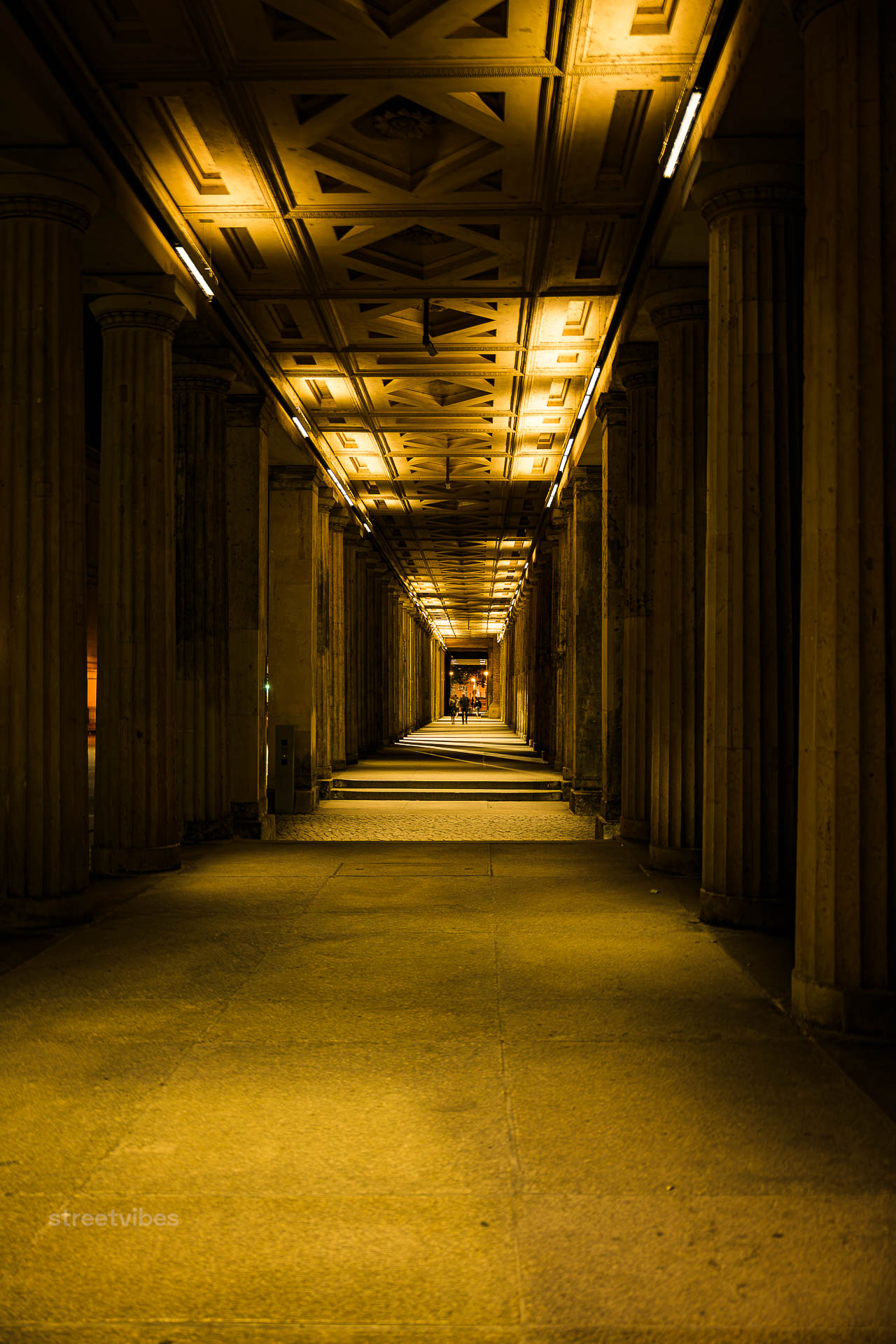 Berlin Unfiltered | Ein langer Flur mit römischen Säulen erinnert an antike Hallen, Villen oder Paläste. Solche Säulengänge (auch Kolonnaden oder Peristyle genannt) dienten im alten Rom der prachtvollen Verbindung von Räumen, boten Schutz vor Sonne und prägten die klassische Architektur durch Symmetrie und feste Ordnungen.